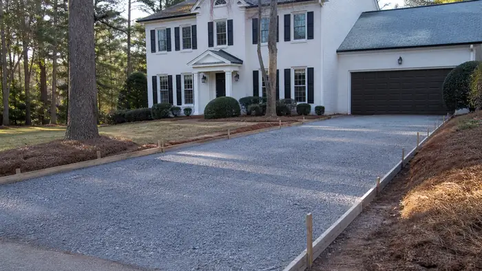 Crushed stone base is raked level inside driveway forms. at a painted-white-brick two-story home in Warner Robins, GA, under low winter sun.
